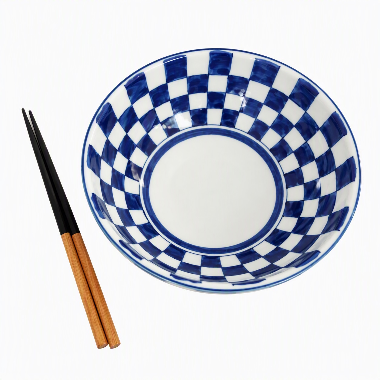 Grand bol japonais à damier en céramique vu de dessus avec une paire de baguettes sur fond blanc