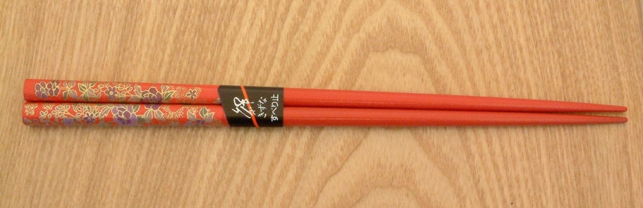 Zoom sur les détails des baguettes japonaises rouges décorées de motifs floraux en bois laqué