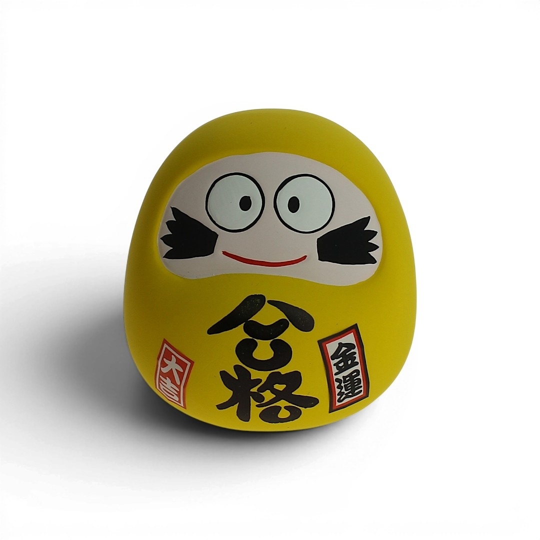 Daruma jaune en céramique vu de face, statuette japonaise porte‑bonheur avec fente tirelire